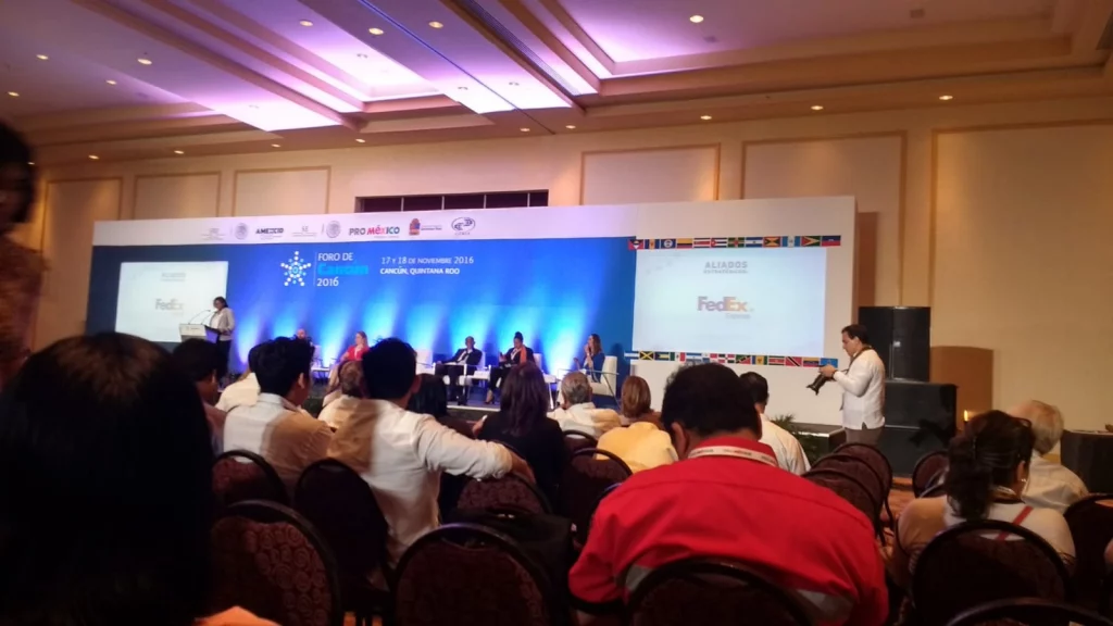 Asistentes en un foro empresarial con panelistas y fondo iluminado en azul.