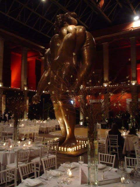 Evento elegante con mesas decoradas y una estatua dorada en el centro del salón.