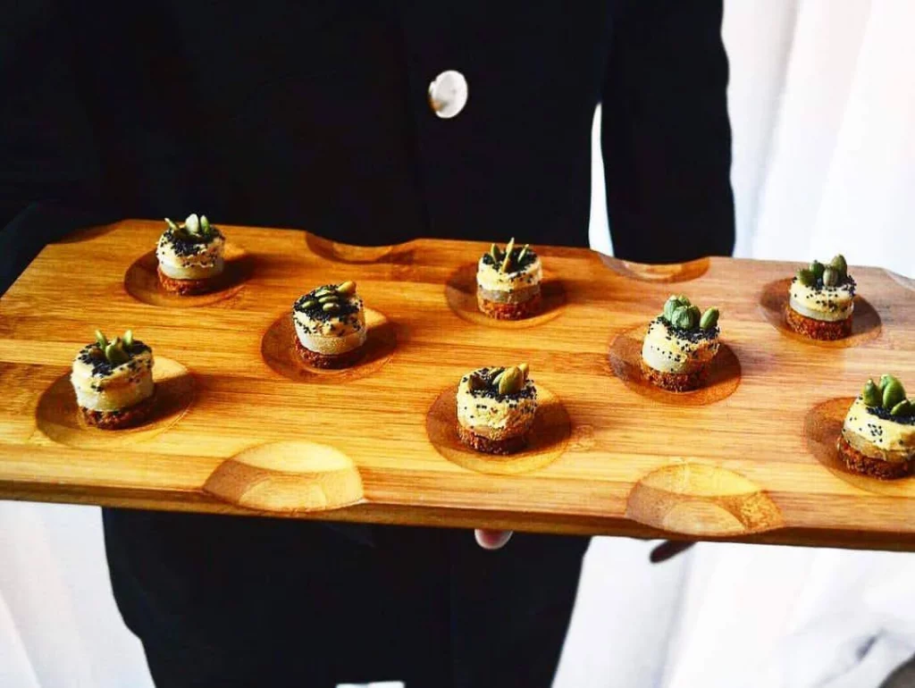 Bandeja de madera con canapés gourmet presentados elegantemente por un mesero.