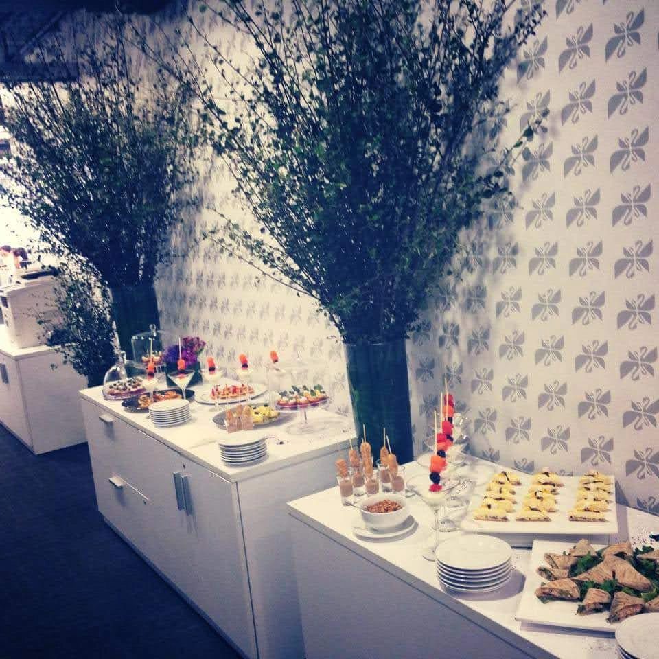 Mesa de buffet con variedad de alimentos, decorada con arreglos florales altos.
