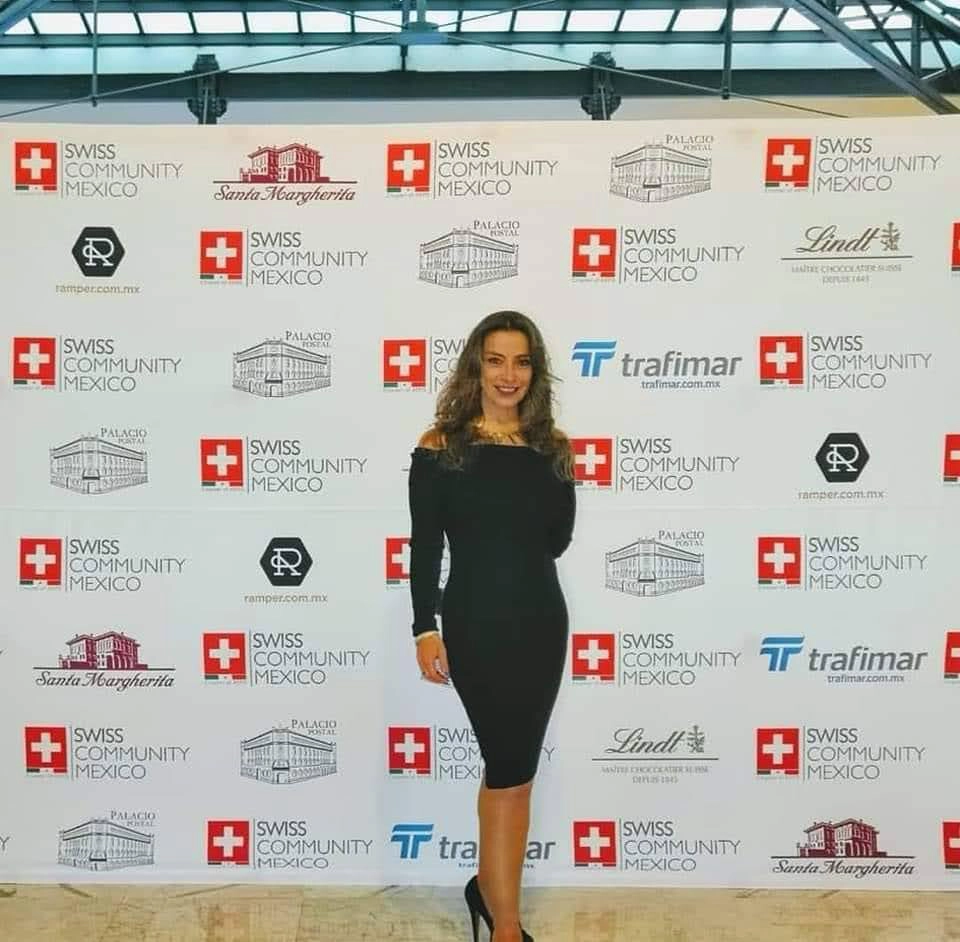 Mujer posando frente a un backdrop con logotipos de patrocinadores en un evento.