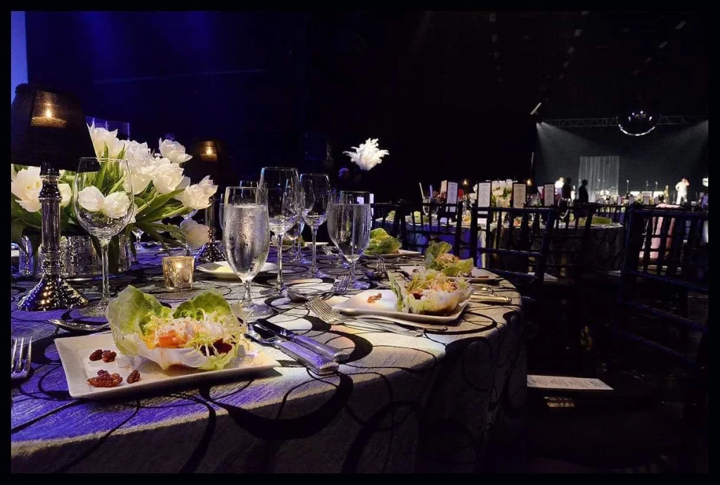 Mesa decorada con flores blancas, copas de cristal y vajilla fina en un evento corporativo.
